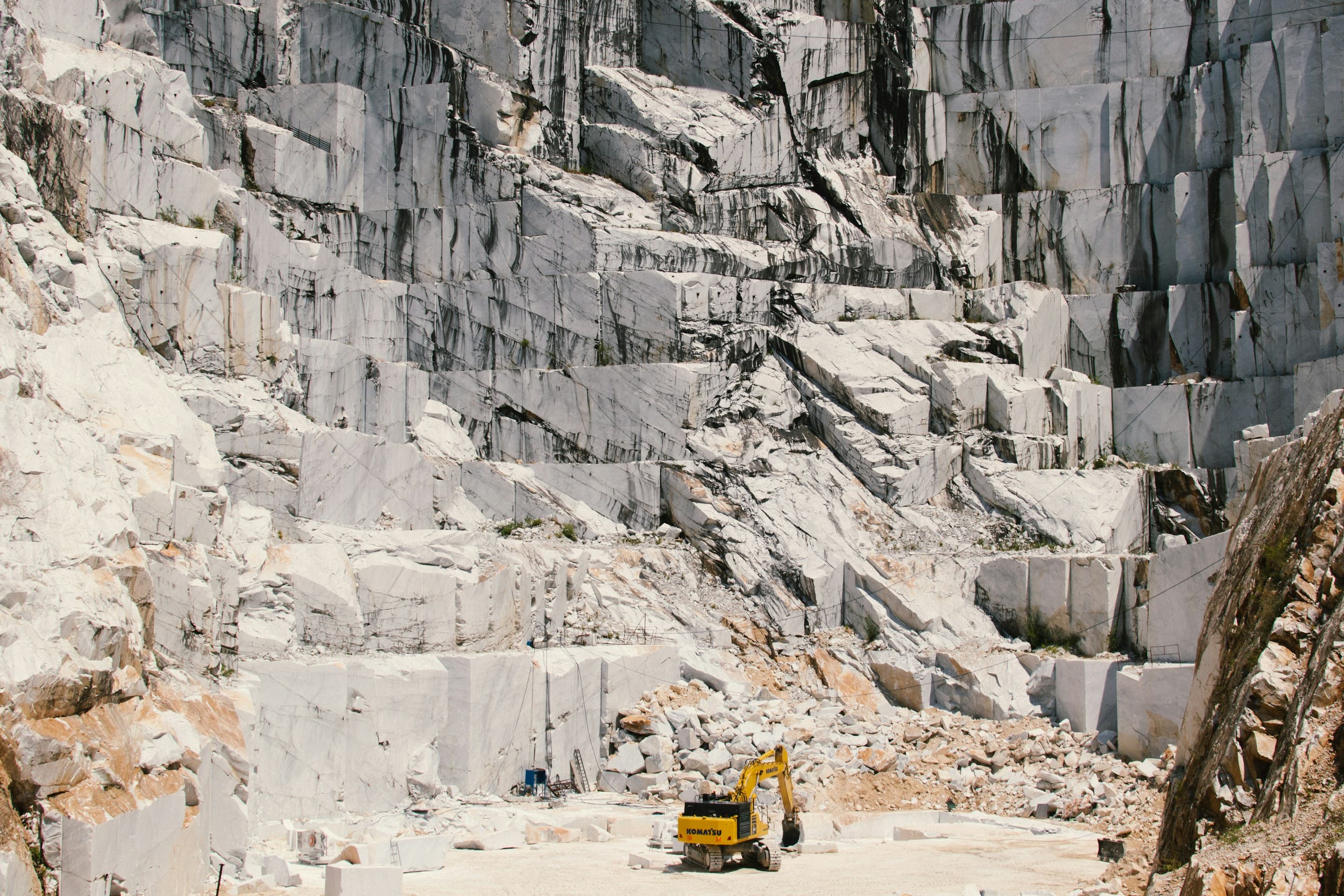 Towering white marble quarry wall with an excavator for scale